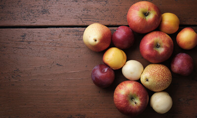 Autumn fruit on a wooden table. Apples, pears, plums, apricots on a dark red background