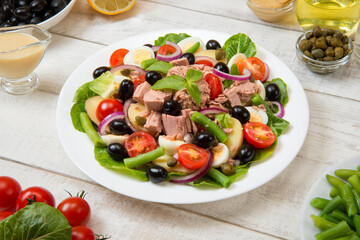 Traditional Nicoise salad in a white plate on a old white table with sauce and ingredients....