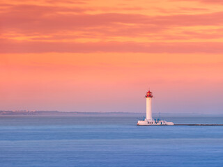 View to alone lighthouse at sea under orange-pink sky in sunset time with copy space