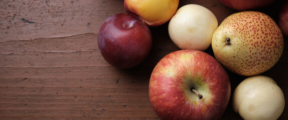 Autumn fruit on a wooden table. Apples, pears, plums, apricots on a dark red background