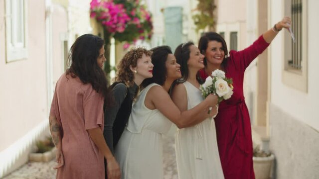 Long shot of bridesmaids taking selfie with lesbian newlyweds. Happy friends taking photo on phone, smiling, posing for camera. Photoshoot, LGBT, wedding ceremony concept