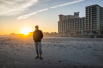 One young man silhouette standing watching colorful sunset at Myrtle Beach city by Atlantic ocean...