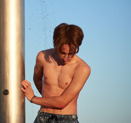 A caucasian male taking a shower at a beach during the day