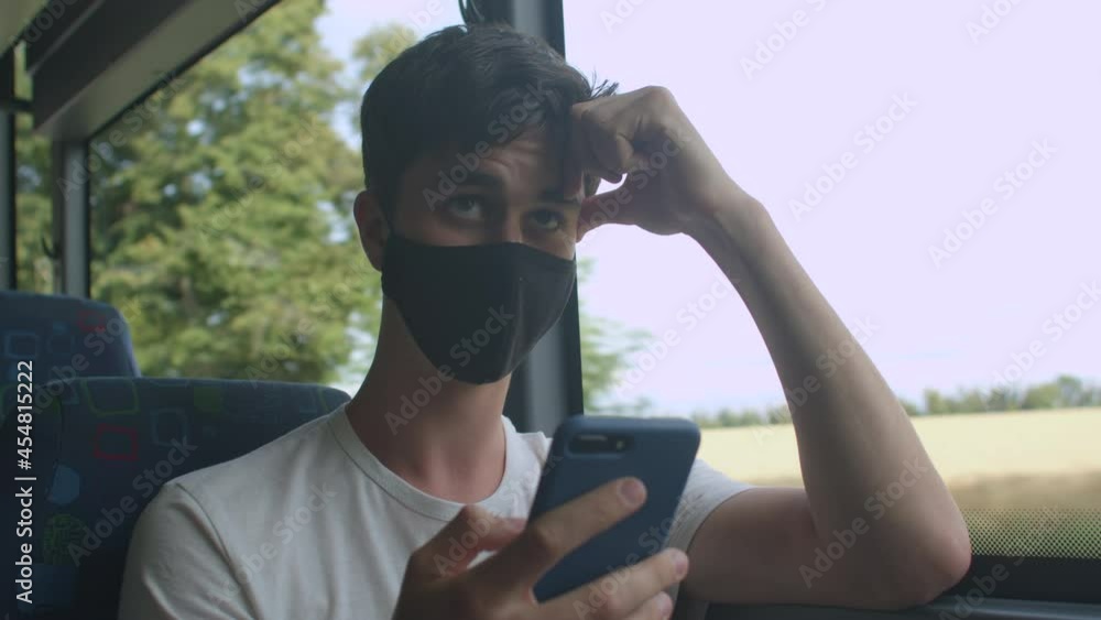 Poster a man in a black mask uses a phone near the bus window in motion. look at the screen along the route