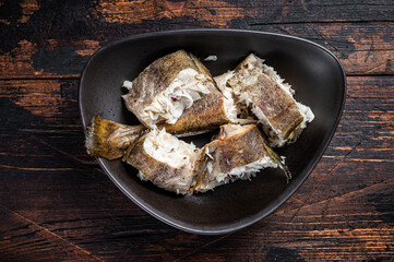 Roasted hake white fish in a plate. Dark wooden background. Top view