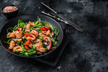 Salmon salad with fish slices, arugula, tomato and green vegetables. Black background. Top View. Copy space