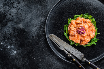 Raw Salmon tartare or tartar with red onion, arugula and capers in black plate. Black background. Top View. Copy space