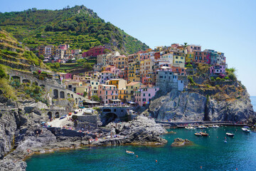 Fototapeta na wymiar Manarola typical Italian village in the National Park of Cinque Terre with colorful multicolored buildings houses on rock cliff, fishing boats on water, Liguria, Italy