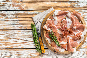 Dry cured parma ham or Prosciutto crudo on a wooden board with rosemary. White wooden background....
