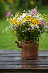 Bouquet of wildflowers with daisies in an old copper teapot on a wooden table outdoors