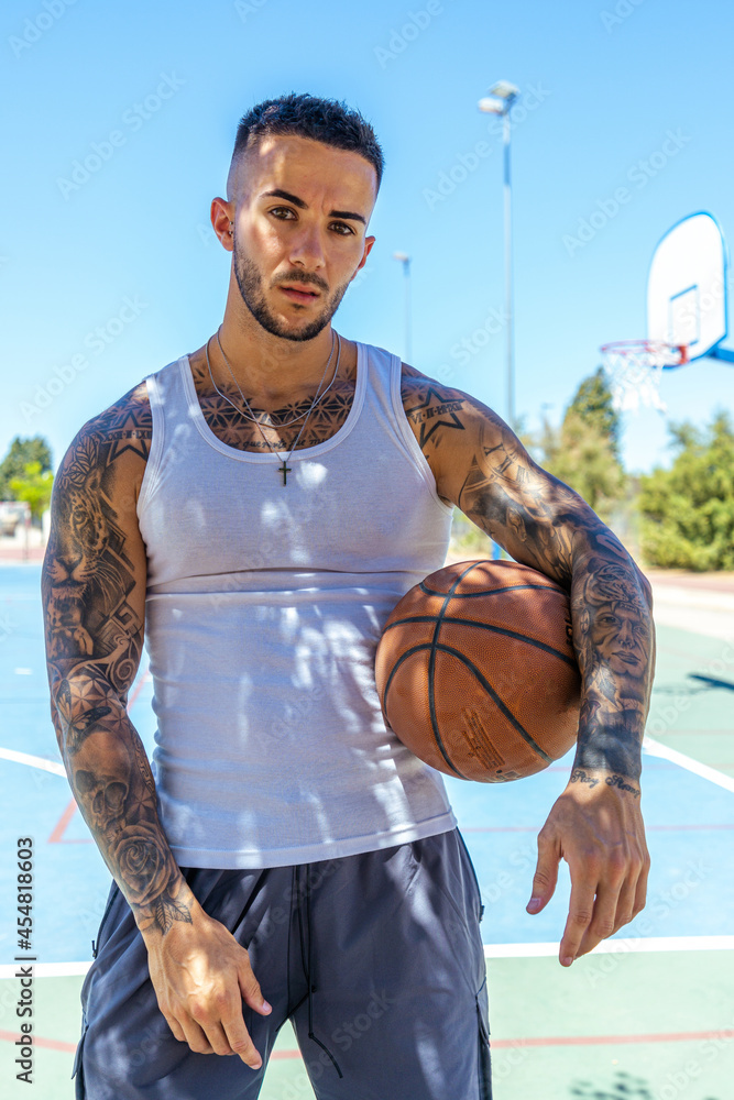 Wall mural vertical shot of a sporty caucasian male with tattoos playing basketball