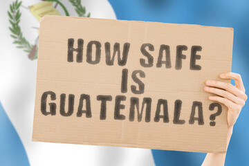 The question " How safe is Guatemala? " on a banner in men's hand with blurred Guatemalan flag on the background. Safety. Street. Outdoor. Dangerous. Security. Attack. Criminal. Criminality