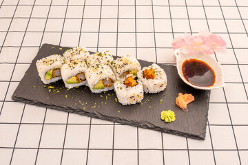 sushi uramaki dragon roll stuffed with shrimp in tempura with ripe avocado, wasabi, ginseng and soy sauce on a slate plate