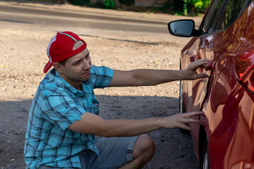 young man examines the dents in his car after the accident; side view