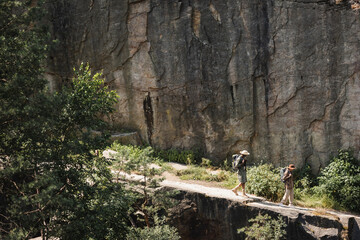 Side view of multiethnic family with backpacks walking near cliff and forest.