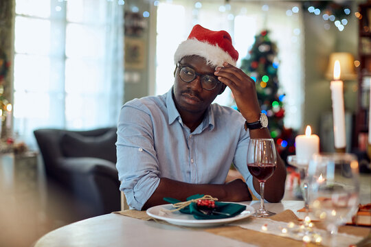 Pensive African American man feels sad while sitting alone at dining table on Christmas.