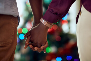 Close-up f black couple holding hands in front of Christmas tree at home.
