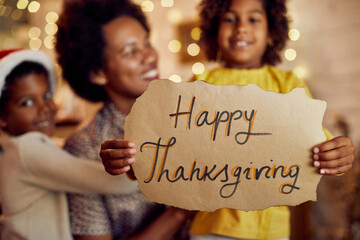 Close-up of black family holds Happy Thanksgiving sign at home.