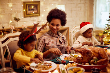 Happy African American mother and her children eat Christmas dinner at dining table.