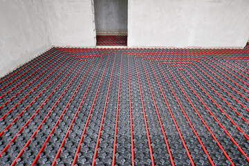 Installation of a heat flooring system in a country house under construction. Red tubes for floor heating. Modern heating system of a country house