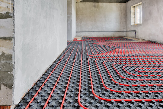 Installation of a heat flooring system in a country house under construction. Red tubes for floor heating. Modern heating system of a country house