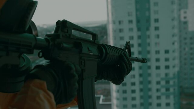 Man in gas mask, a protective suit, with a weapon stands on edge of high-rise unfinished building and sharply aims. Atmosphere of the post-apocalypse, the consequences of man-made disaster, pandemic.