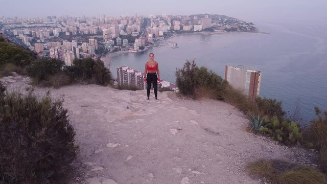 Video 4K de deportista haciendo ejercicio de b&iacute;ceps con mancuerna en lo alto de la monta&ntilde;a con vistas a la ciudad y al mar.