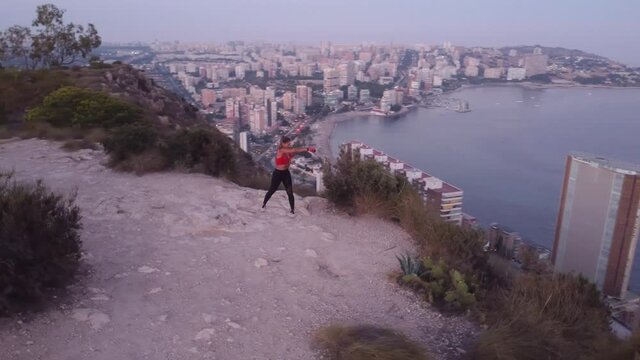 Video 4K, de deportista haciendo ejercicio de boxeo, en lo alto de una monta&ntilde;a con vistas a la ciudad y al mar.
