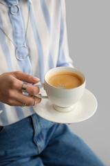 Woman drinking tasty coffee on grey background, closeup
