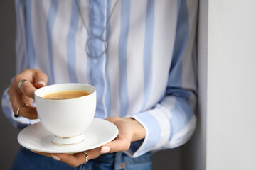 Woman drinking tasty coffee near light wall, closeup