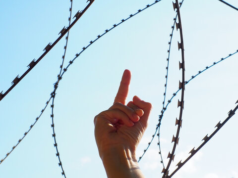 Hand shows middle finger against the background of barbed wire and blue sky