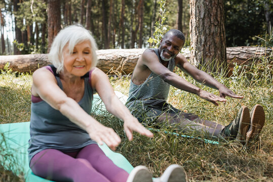 Smiling african american man training on fitness mat near senior wife in forest.