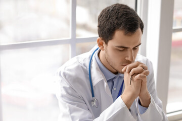 Religious doctor praying in clinic