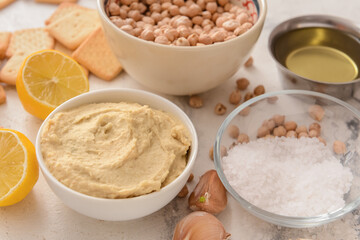 Bowl with tasty hummus and ingredients on light background