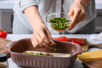 Woman preparing tasty vegetable lasagna at table in kitchen, closeup