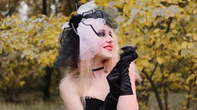 A beautiful girl in the image of a witch in black gloves with black eyes and red lips. Scares, smiles.
Halloween, autumn holiday concept. Slow motion, 4k footage 