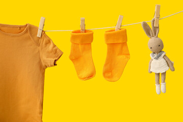 Baby clothes and toy hanging on rope against color background