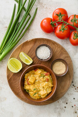 Bowl of tasty chicken curry and ingredients on light background