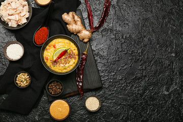 Bowl of tasty chicken curry and ingredients on dark background