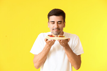 Young man with tasty sandwich on color background