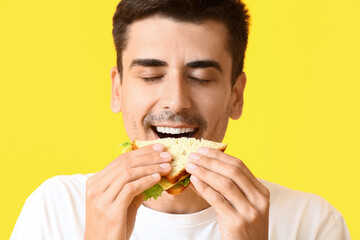 Young man eating tasty sandwich on color background