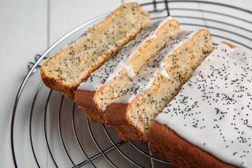 Cooling grid with delicious glazed poppy seed cake on white wooden table, closeup