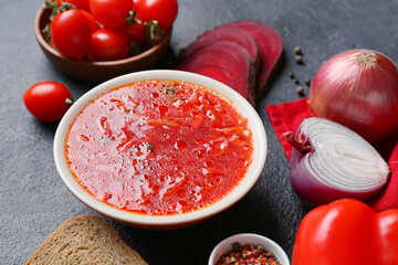 Bowl of tasty borscht and ingredients on dark background