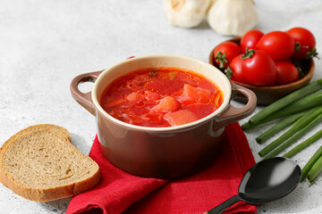 Pot of tasty borscht and ingredients on light background