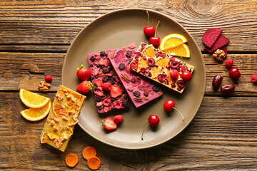 Handmade chocolate bars with fruits, berries and nuts on wooden background