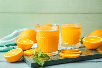 Fototapeta na wymiar Board with glasses of tasty orange juice on color wooden background, closeup