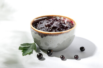 Bowl with black currant jam on white background