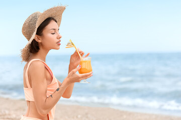 Beautiful young woman drinking cocktail on sea beach