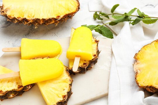 Board with tasty pineapple popsicles on light background