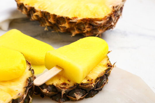 Board with tasty pineapple popsicles on light background